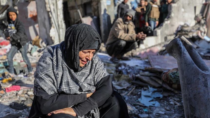 A woman sits amongst damaged homes caused by Israeli air strikes, on January 18, 2024 in Rafah, Gaza.