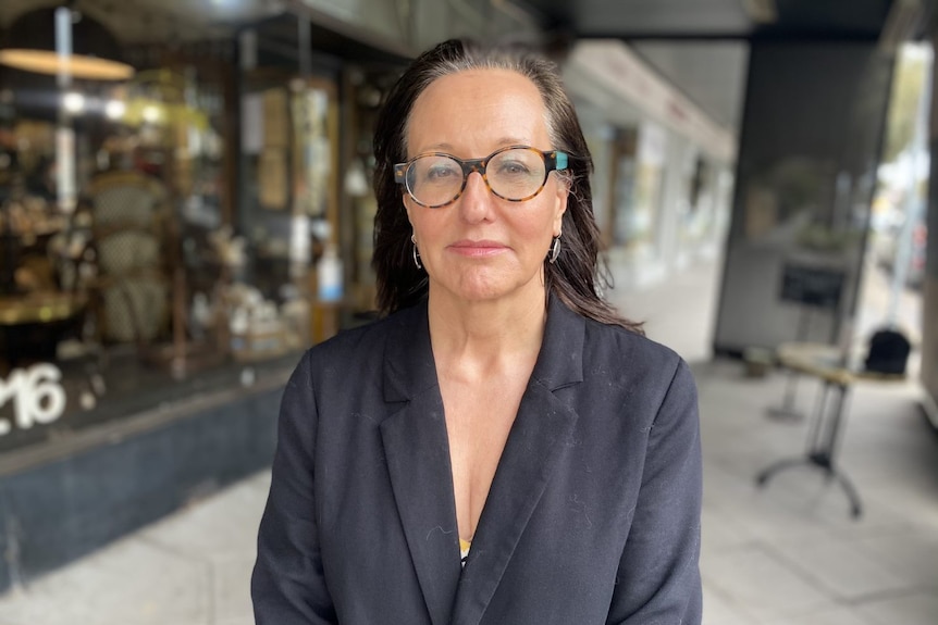 Dr Zena Burgess stands in front of a closed cafe with a serious expression