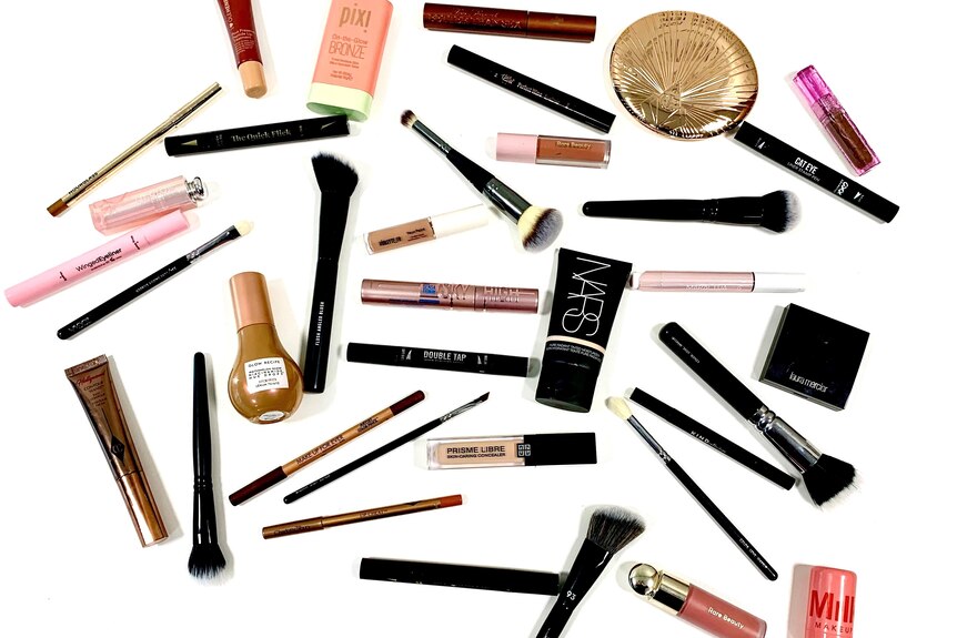 A birds eye view of beauty products and makeup brushes scattered across a white background.