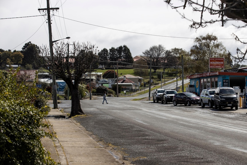 Cars lining the street on the Lyell Highway in Ouse, near the Roadhouse Takeaway. A person crosses the road. 