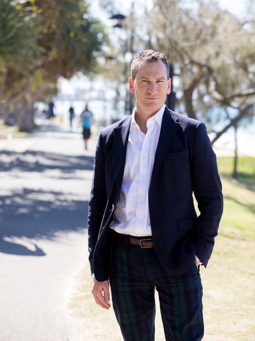 A man stands on a coastal footpath with trees in the background.