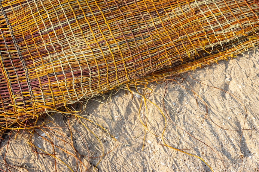 A large colourful woven mat is laying on a sandy beach at twilight.