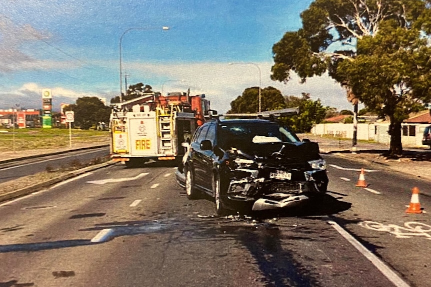 A damaged black car on a road with a fire truck