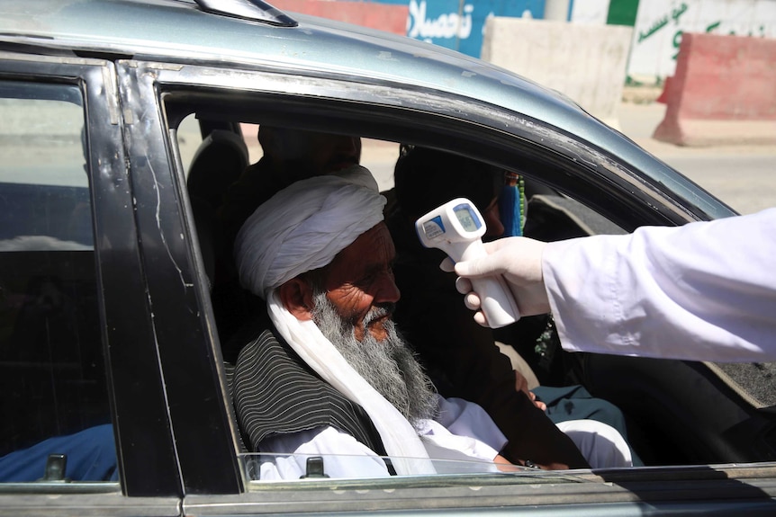 A health worker checks the temperature of an elderly man wearing a turban in a car.