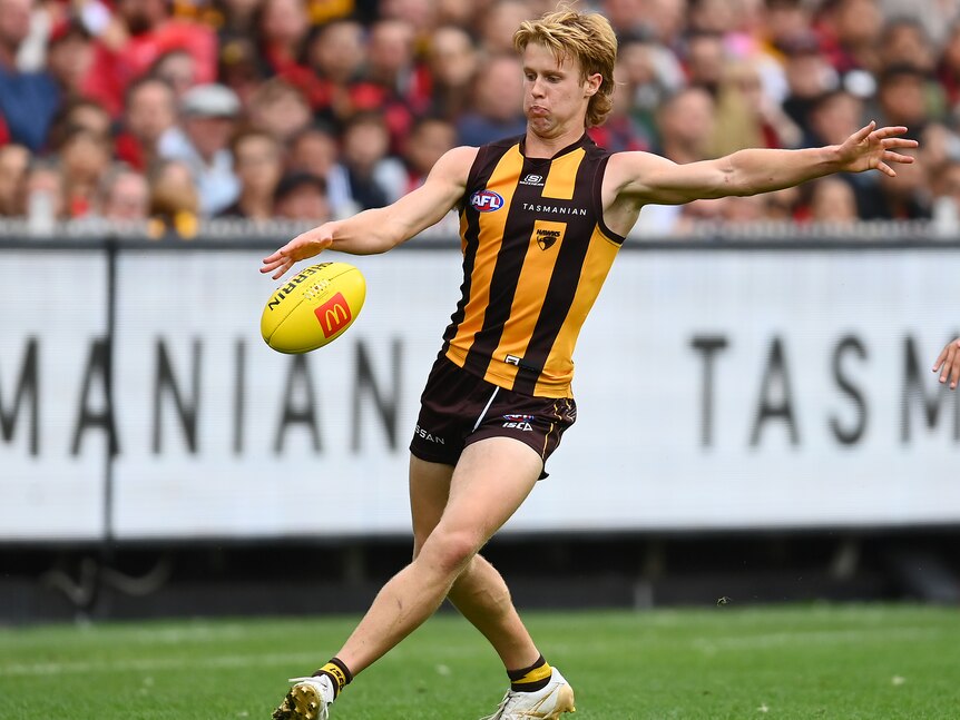 A young Hawthorn midfielder looks down at the ball as he prepares to kick it downfield during his debut game.