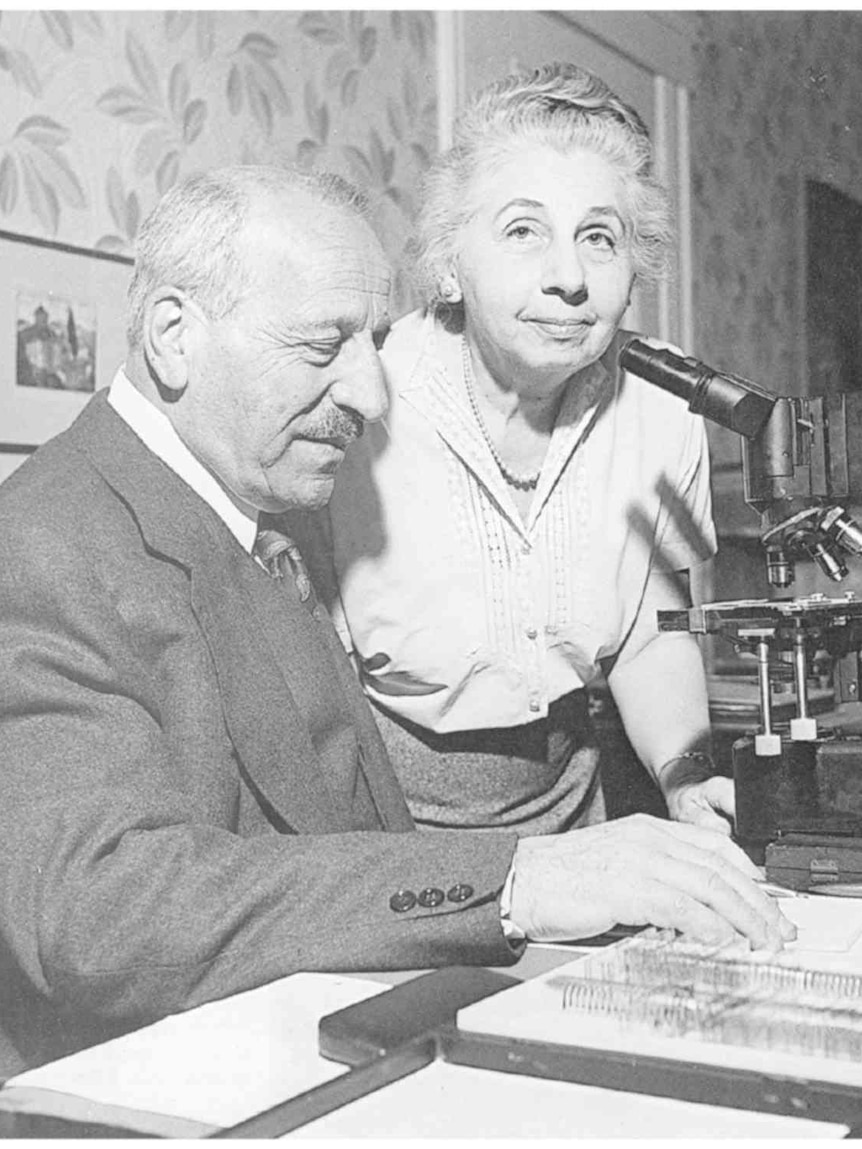A black and white photo of an older man and woman with a microscope