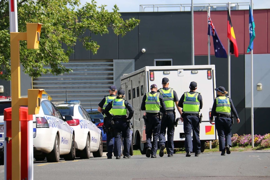 Police officers walk towards a white prison van