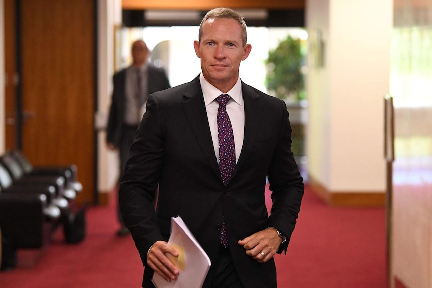 Mick de Brenni walks down a hallway holding papers at Parliament House in Brisbane.