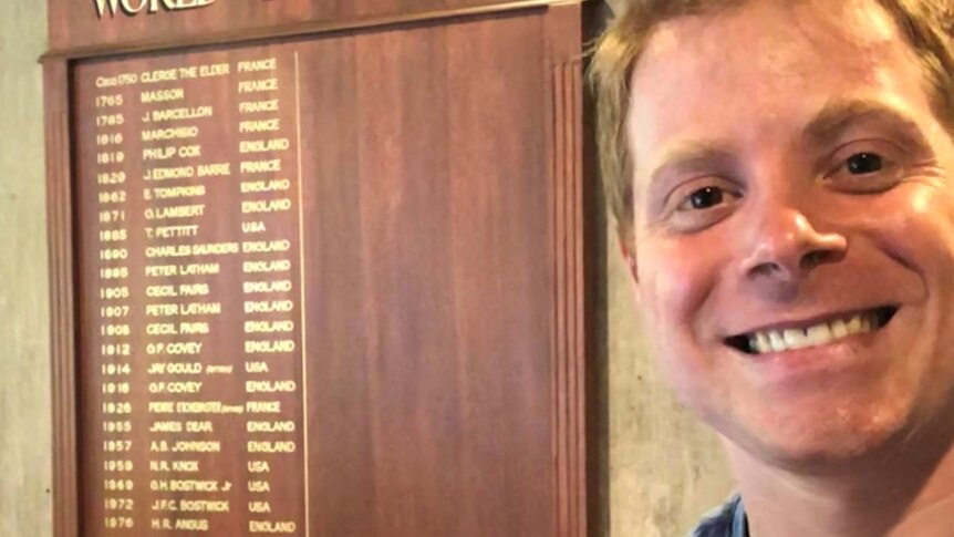 A man smiles in front of a list of world champions where he features