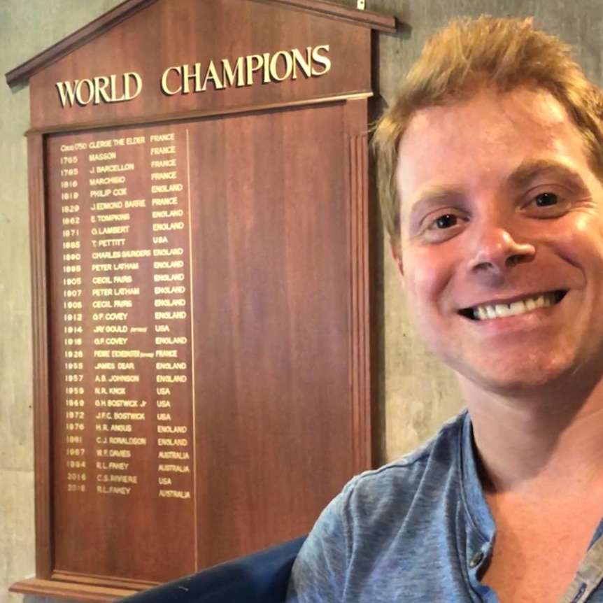 A man smiles in front of a list of world champions where he features