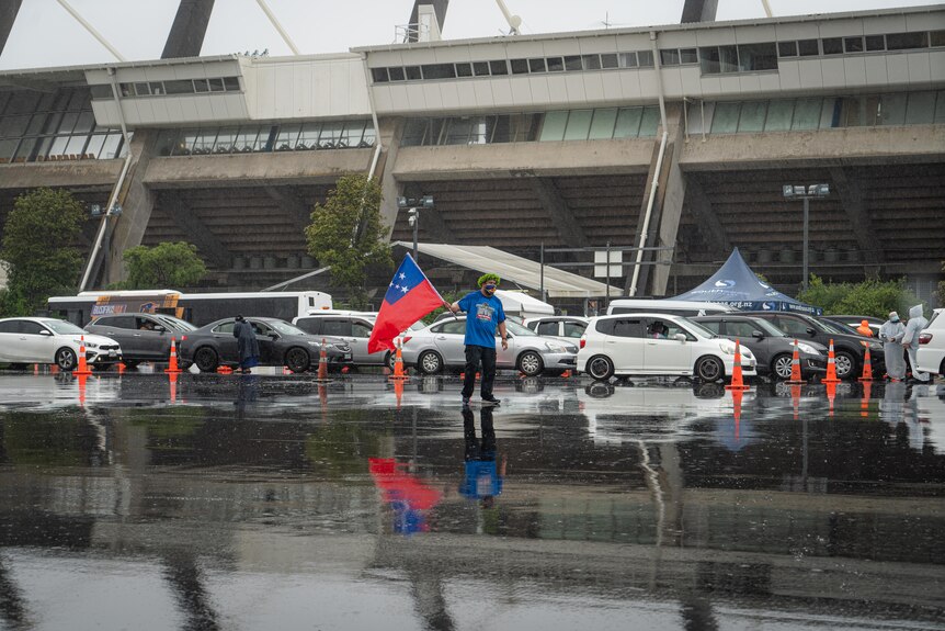 A man waves a Samoan flag as people line up in their cars to be vaccinated.  