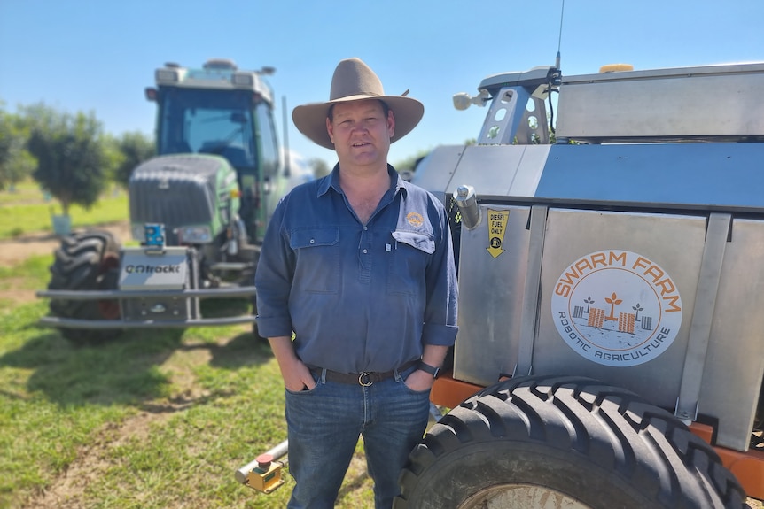 A man stands in a paddock in front of a tractor near another machine.