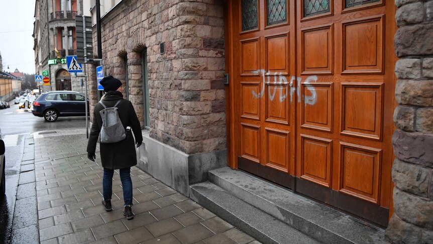 A person walks past a house on a street that has the word "Judas" sprayed on the wooden front door.