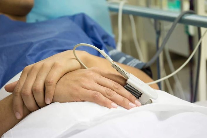 Unidentified woman's hands as she lays on a surgical bed as a patient while her heart rate is being monitored. 