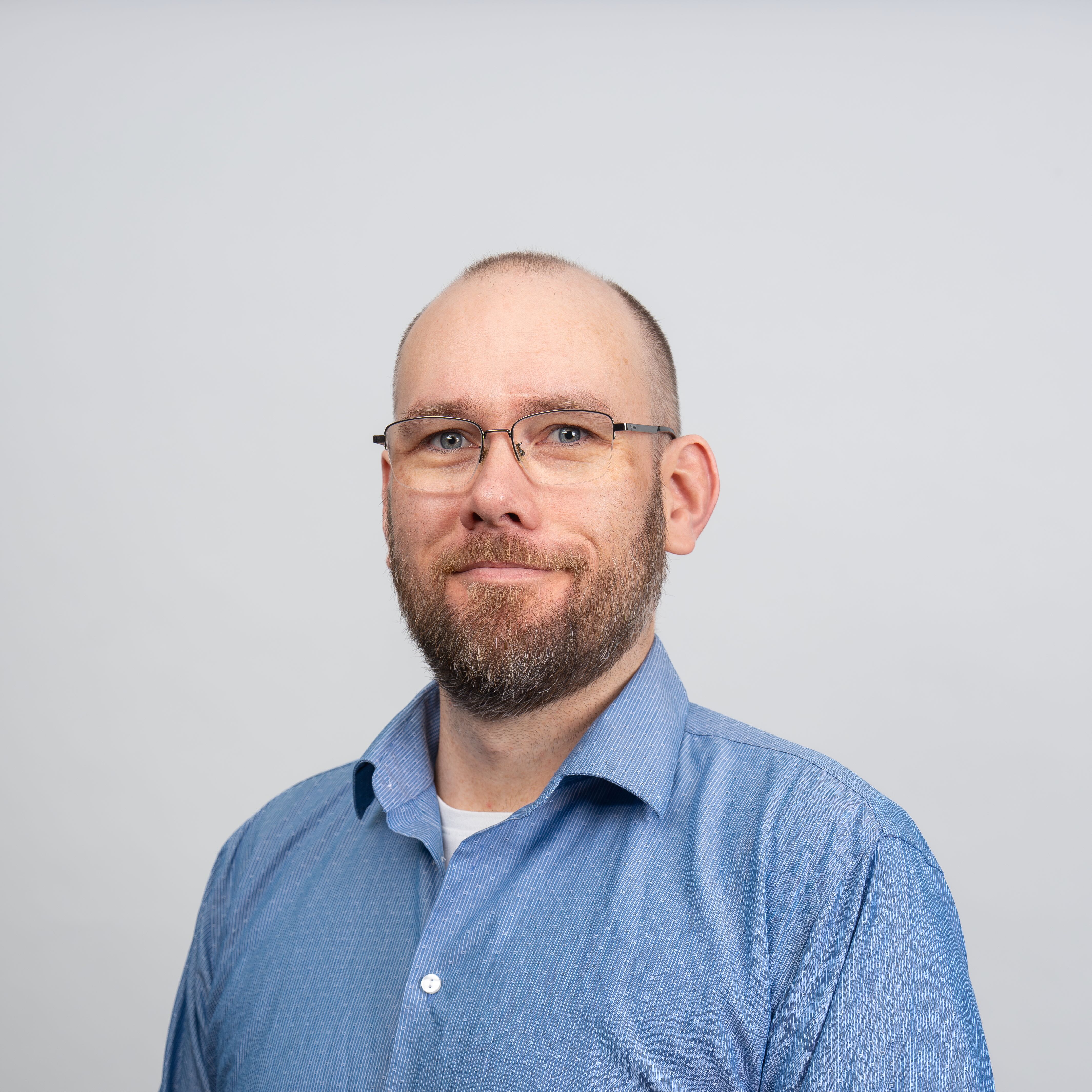 A man with a beard and glasses smiles towards the camera.
