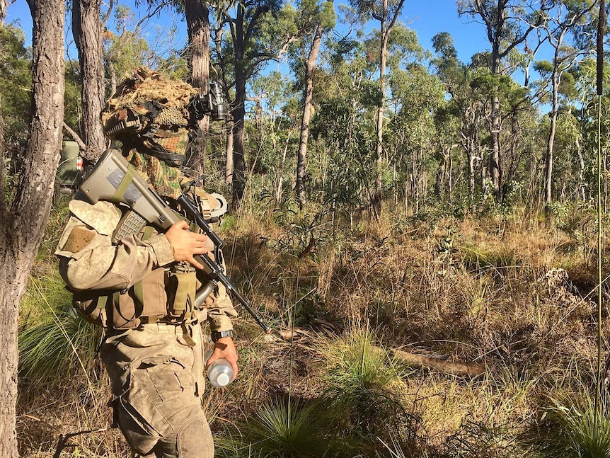 A New Zealand soldier is covered head to toe in camouflage gear, blends in well with bushland