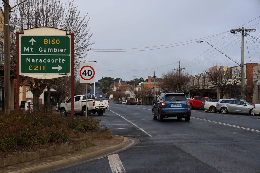 A car drives past a sign pointing the directions to travel for Mount Gambier and Naracoorte on a built up street