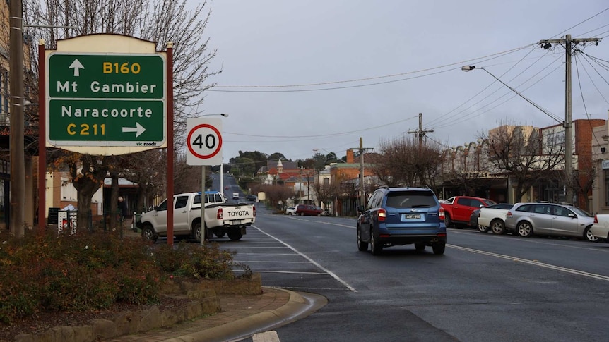 A car drives past a sign pointing the directions to travel for Mount Gambier and Naracoorte on a built up street