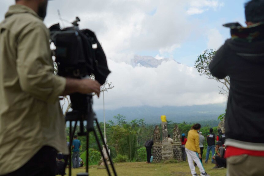 People stand around and take photos of Mount Agung.