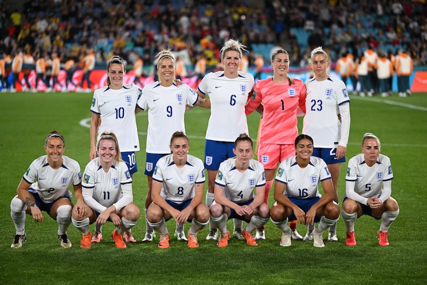 11 female soccer players, five standing and the rest crouching, pose for a group photo on the pitch.
