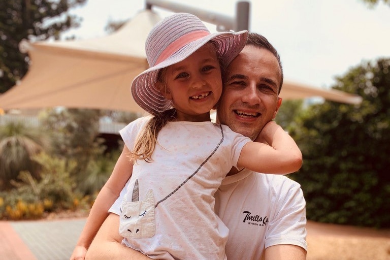 Shot of father carrying daughter who is wearing wide-brim hat, both are smiling