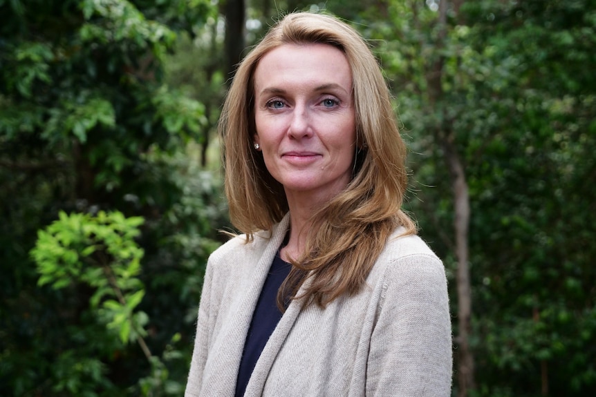 A woman looks neutrally in front of green leaves of a forest