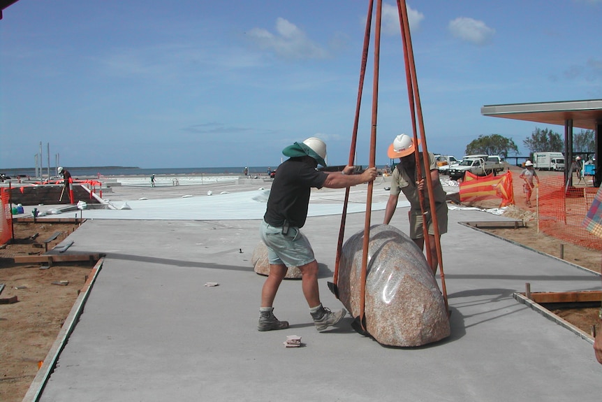Two men load a big rock on to a device to lift it