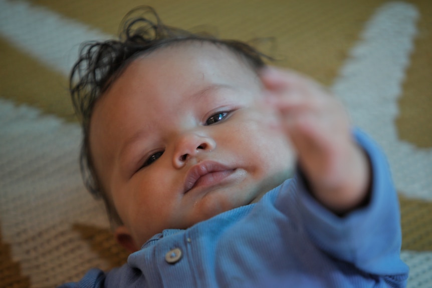 A baby reaches a hand up.