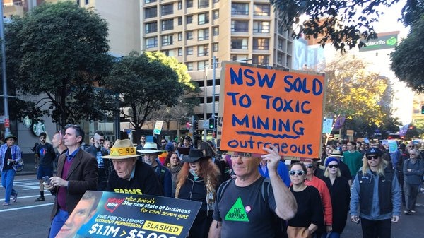 A man with an anti-mining sign marches at the front of a crowd.