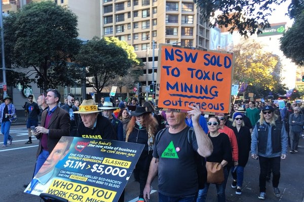 A man with an anti-mining sign marches at the front of a crowd.
