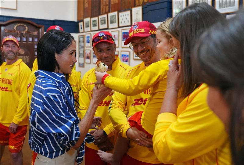 Meghan grabs a toy bear being given to her by a young girl in a surf life saving uniform.