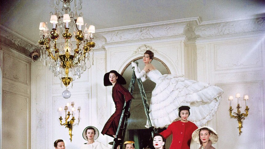Women in dresses stand around a couch and a ladder while posing for a photo