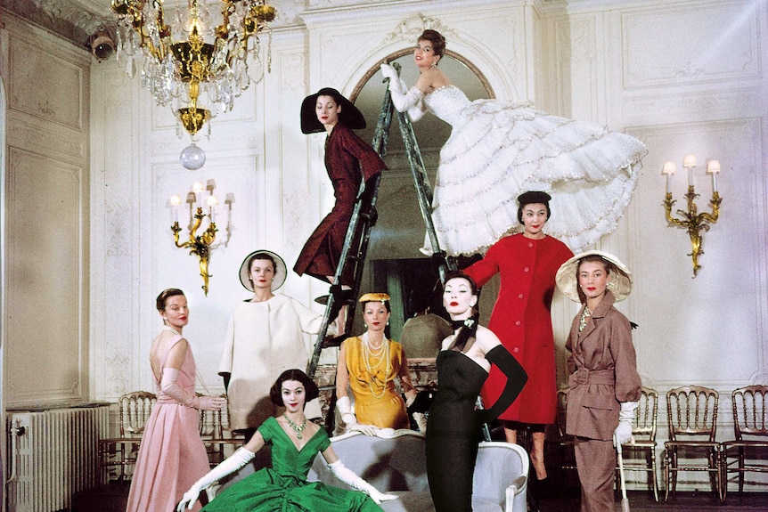 Women in dresses stand around a couch and a ladder while posing for a photo