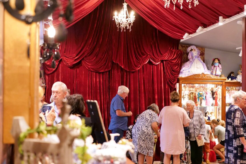 People talking and drinking inside a doll museum which is decorated in red velvet and chandelier.