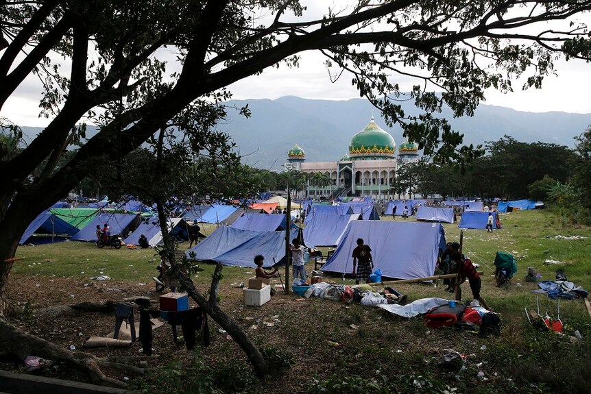 A field is full or rudimentary blue tents and people, near a mosque