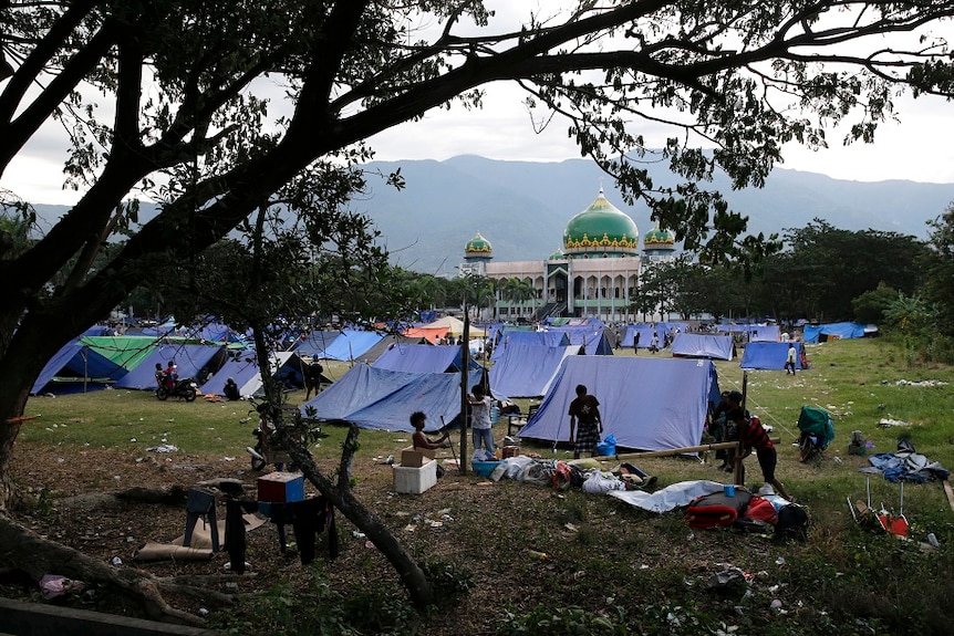 A field is full or rudimentary blue tents and people, near a mosque