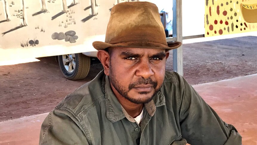 An Indigenous Australian man in a leather hat looks at the camera