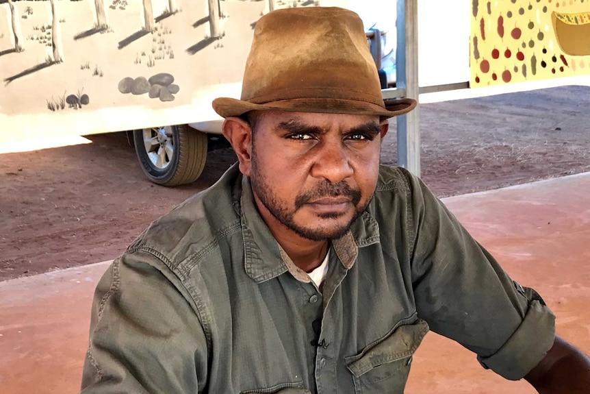 An Indigenous Australian man in a leather hat looks at the camera