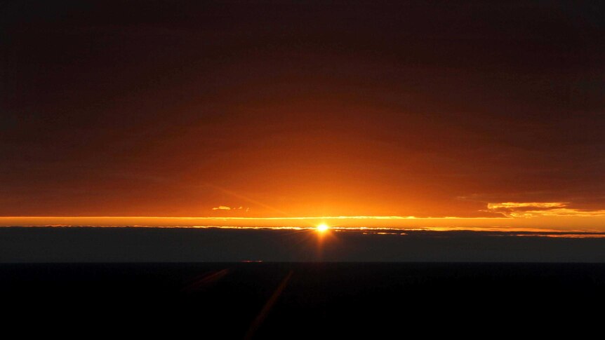 The first rays of sunlight break between two layers of cloud.