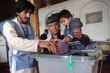 A man holds his child as he places his ballot paper in a voting box.
