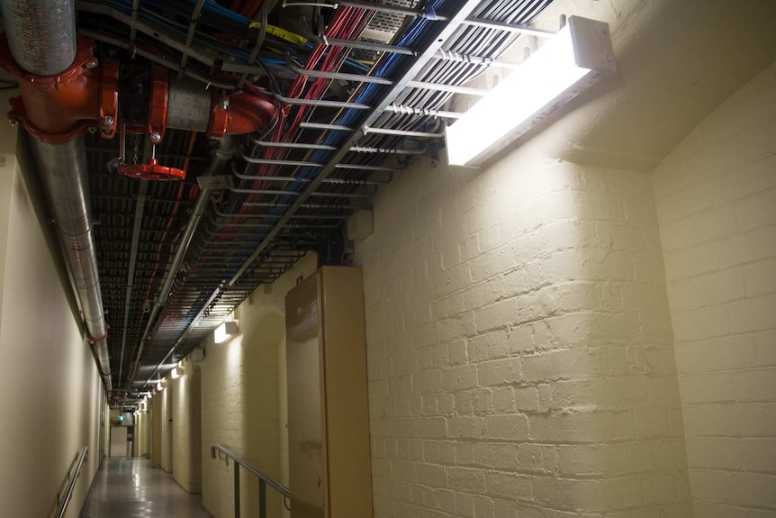 A corridor with brick alcoves, water pipes and cabling.