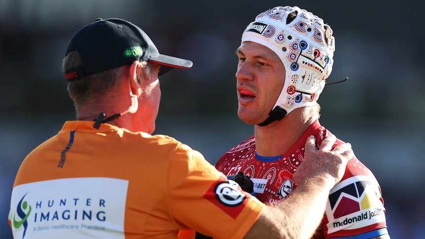 NRl star Kalyn Ponga looks at a trainer who has his hand on his shoulder as he checks him after a knock.