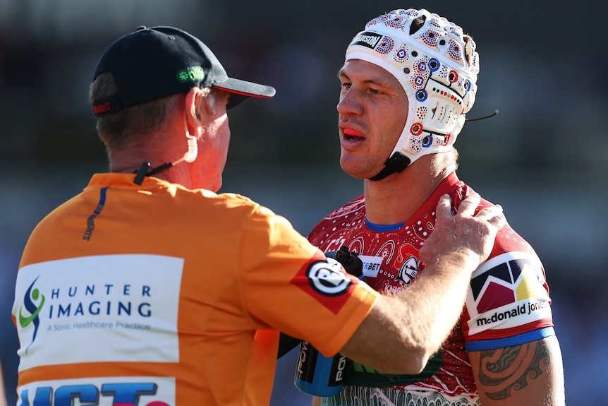 NRl star Kalyn Ponga looks at a trainer who has his hand on his shoulder as he checks him after a knock.