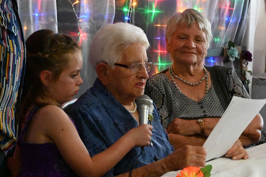 Lady sits at a birthday table speaking to friends and family.