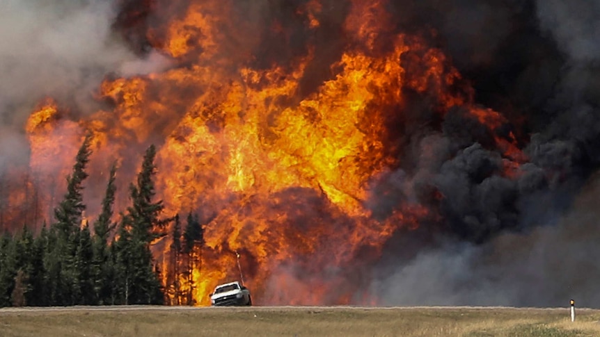 Smoke and flames from the wildfires erupt behind a car