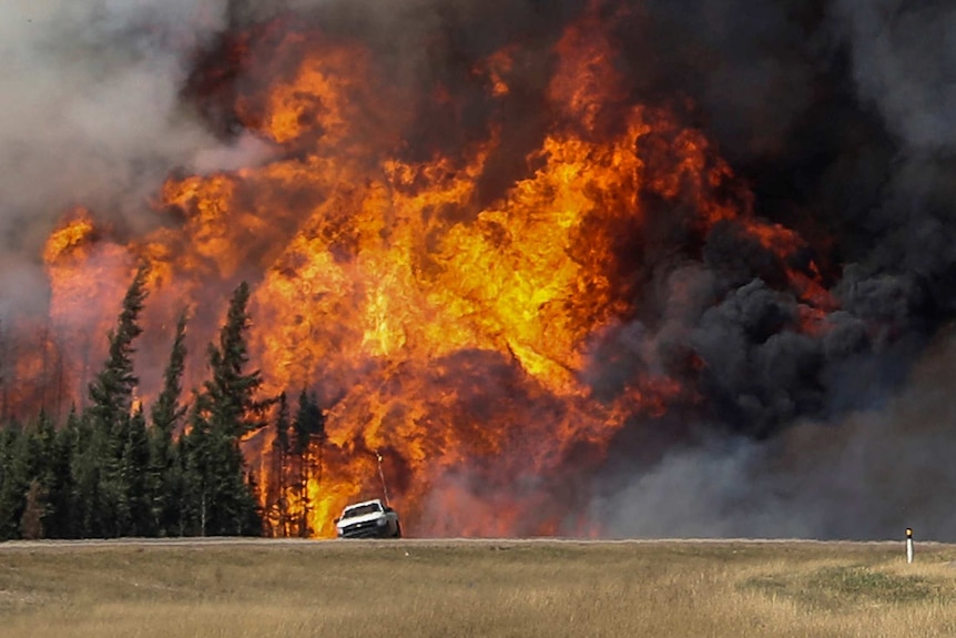 Smoke and flames from the wildfires erupt behind a car