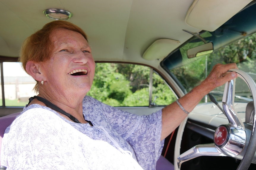 Woman smiles as she rests her hand on the steering wheel of a vintage holden car