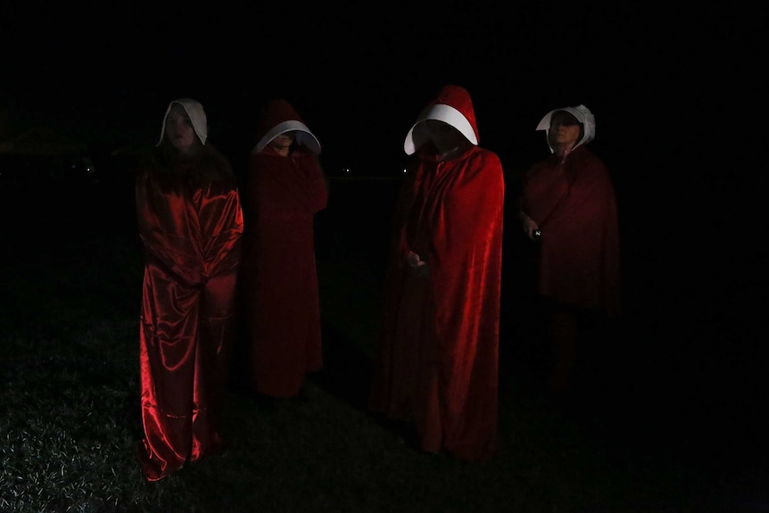 Four women wear red cloaks and hoods, in the style of Margaret Atwood's novel 'The Handmaid's Tale'.