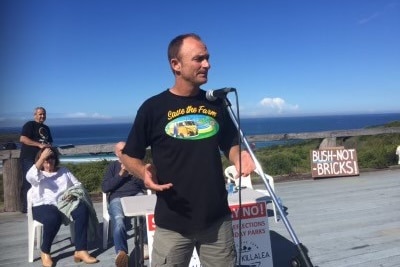 A man wearing 'Save the Farm' t-shirt stands in front of microphone