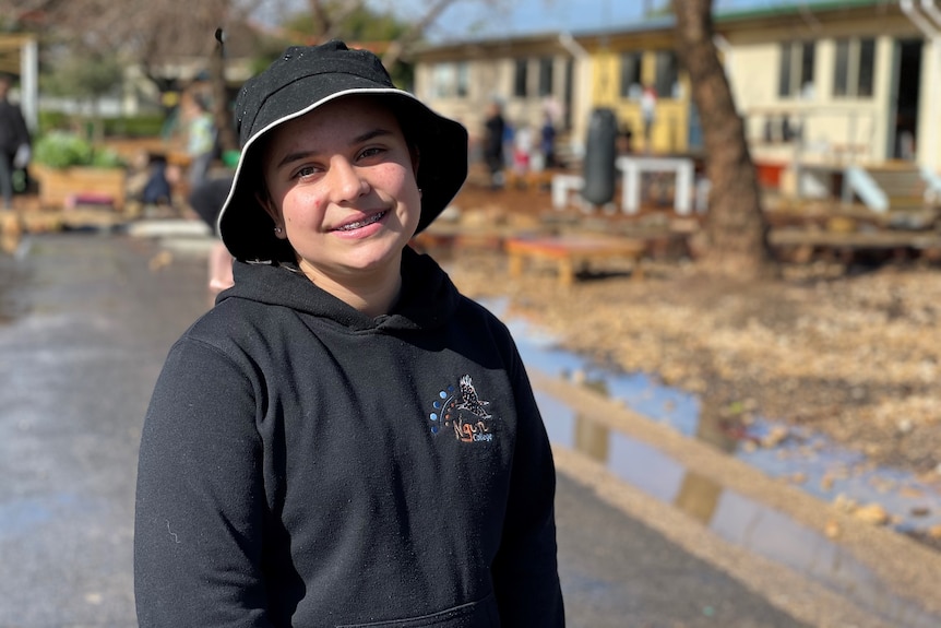 A girl wearing a black bucket hat and dark school jumper smiles at the camera